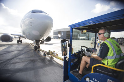a man in a blue vehicle with a large airplane behind him